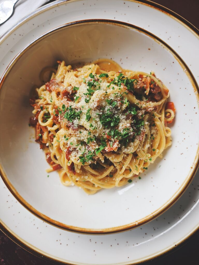 Bowl of long pasta in a tomato sauce topped with grated parmesan and fresh herbs served at Camp West