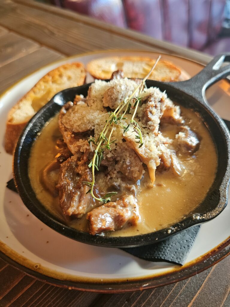 Cast-iron skillet of braised meat and mushrooms in creamy sauce with toasted crostini at Camp West