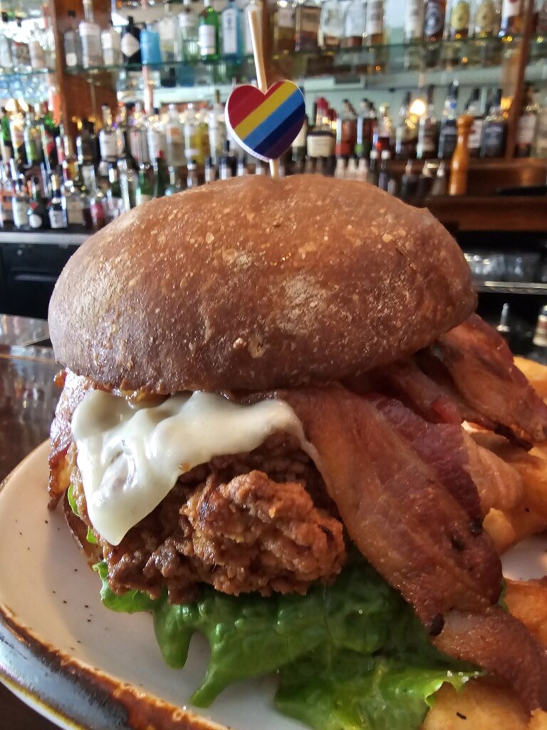 Bacon cheeseburger with a dark bun and crisp lettuce at Camp West in West Seattle with the bar behind it