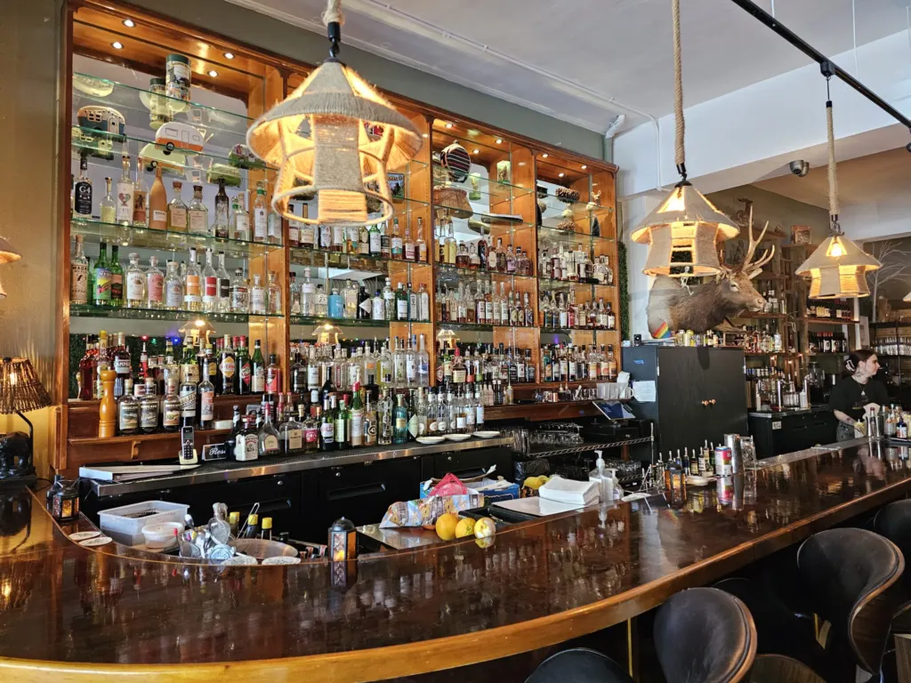 Camp West's bar in the West Seattle Junction with a curved wood bar top, lit liquor shelves, rope pendant lamps and a mounted elk head