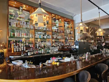 Camp West's bar in the West Seattle Junction with a curved wood bar top, lit liquor shelves, rope pendant lamps and a mounted elk head