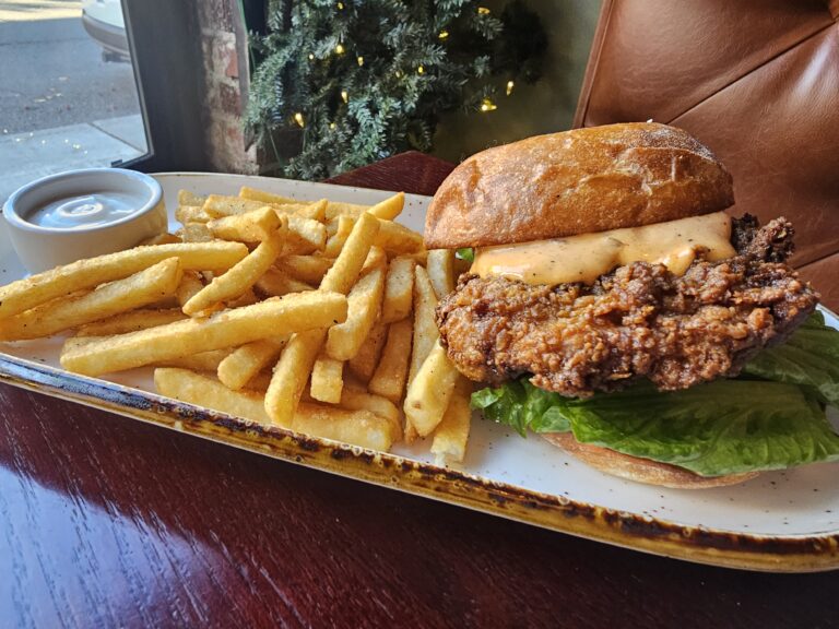 Crispy fried chicken sandwich on a brioche bun with lettuce and sauce served with fries at Camp West