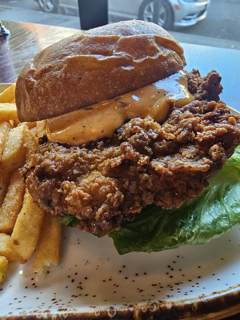 Close-up of a crispy fried chicken sandwich with sauce on a brioche bun served with fries at Camp West