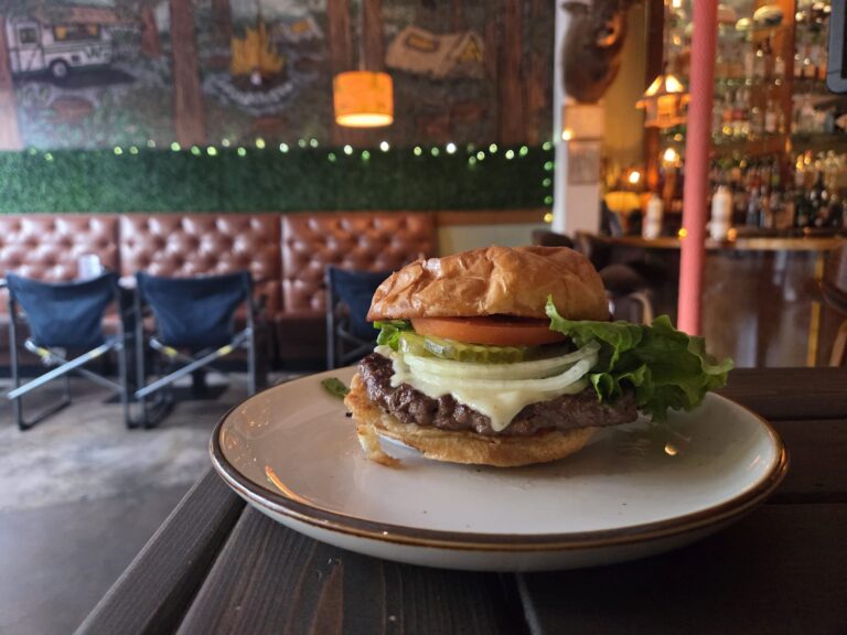 Smash burger with melted cheese, tomato, onion and lettuce on a brioche bun plated in the Camp West dining room