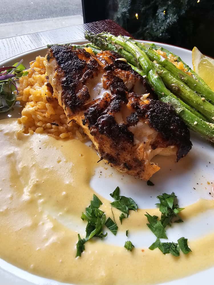 Blackened fish fillet in cream sauce with saffron rice and asparagus on a white plate at Camp West